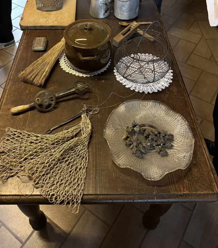 Il tavolo della cucina con una rete, una scopetta di saggina, una pentola, un frullino e un piatto di vetro