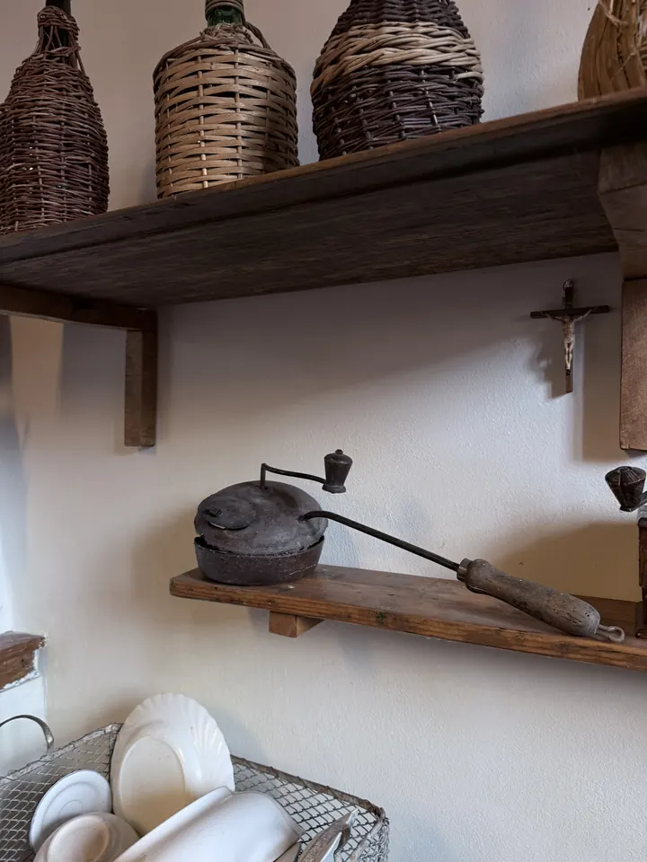 Il tostacaffè con il lungo manico di legno appoggiato sulla mensola, sopra una rastrelliera di piatti