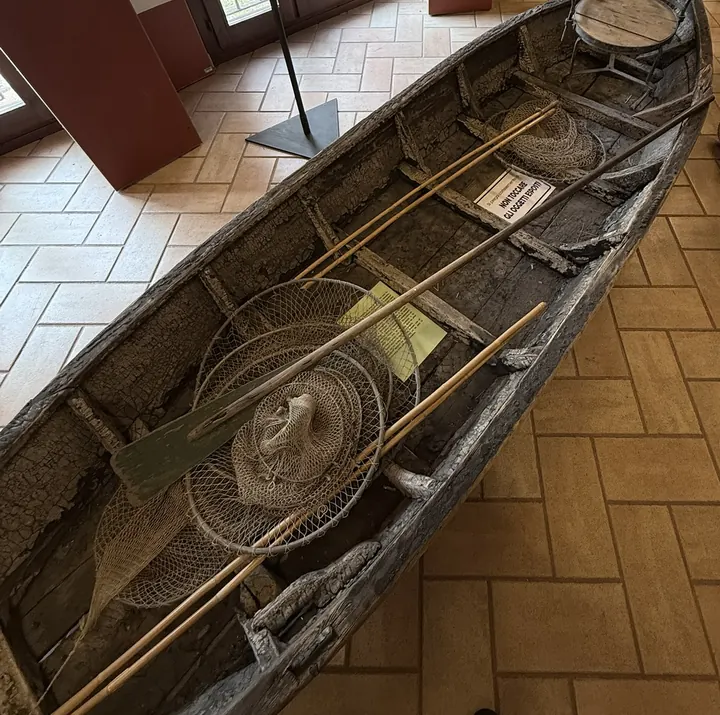La barca da pesca piatta e stretta, con le reti e i remi, accanto al pannello «La caccia»