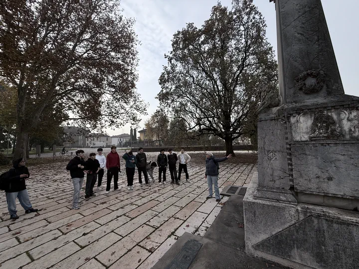 La classe radunata su una piazza lastricata accanto alla base di un monumento, sotto gli alberi d’autunno