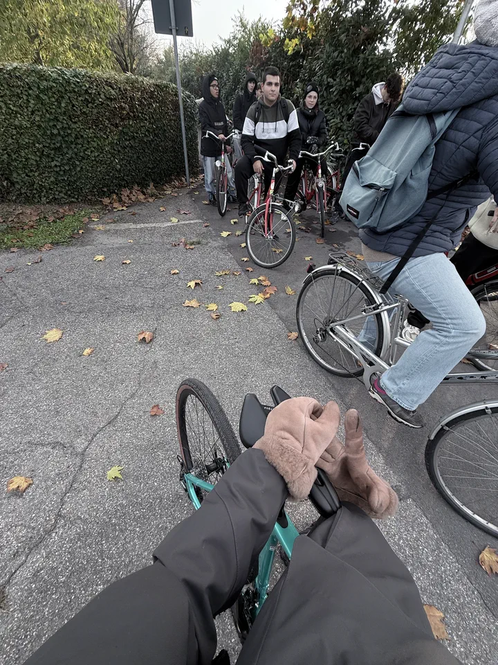La strada vista dal manubrio: la mano sul freno e i compagni in bicicletta dietro