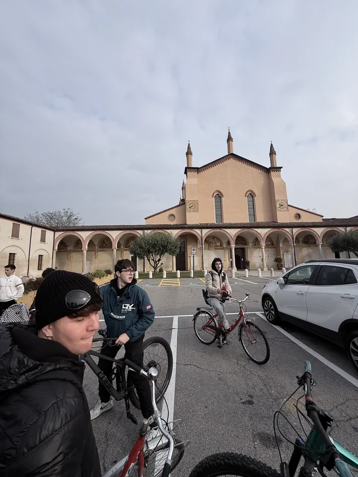 Compagni in bicicletta sulla piazza del santuario delle Grazie, con il portico e la facciata della chiesa