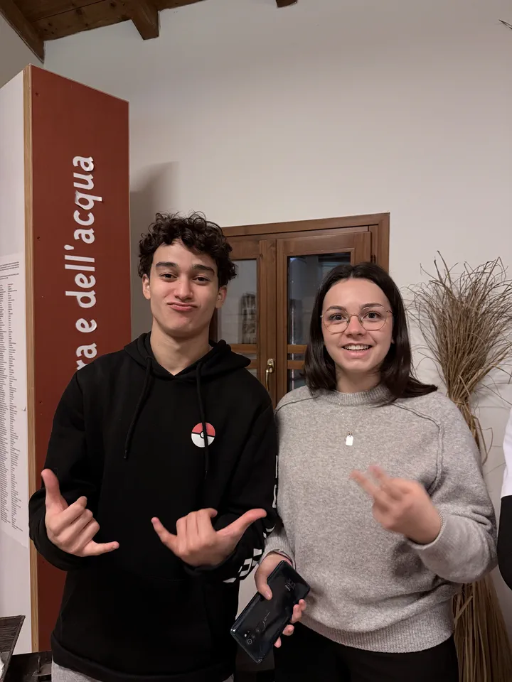 Due compagni di classe in posa davanti a un pannello rosso del museo e a un fascio di canne